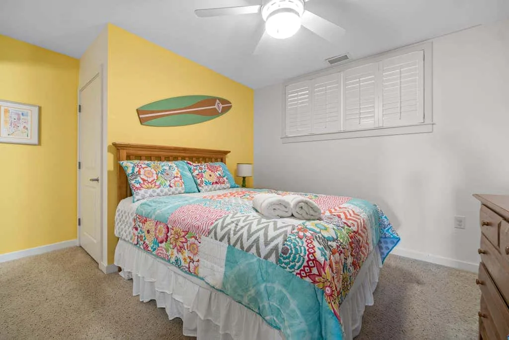 Un dormitorio con una colcha colorida estampada y un ventilador de techo.