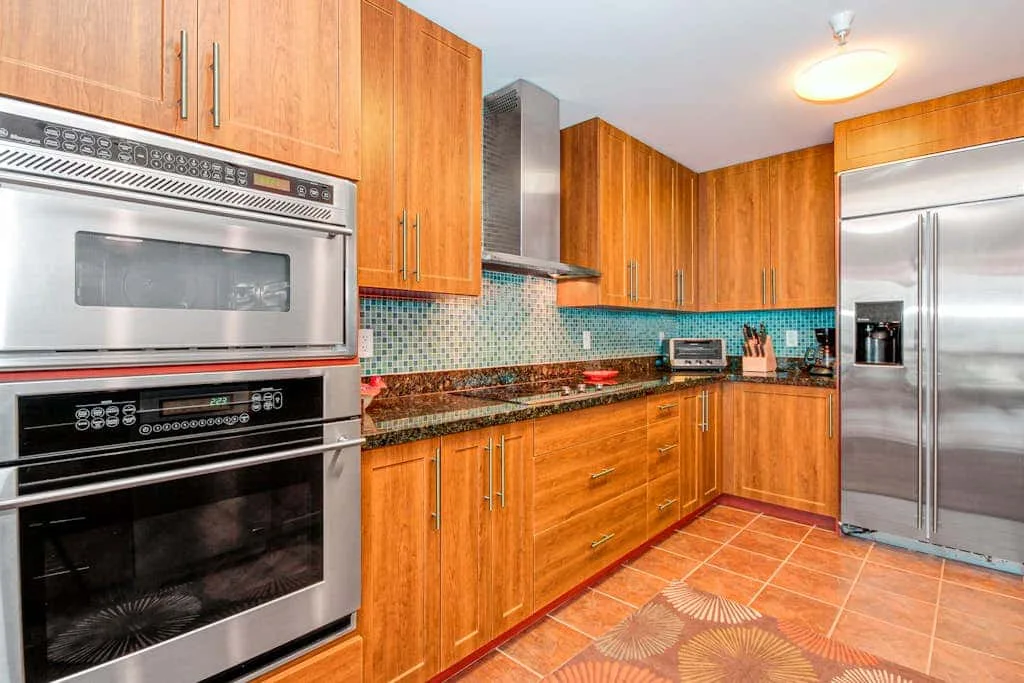 Una cocina con gabinetes de madera, electrodomésticos de acero inoxidable y piso de baldosas.