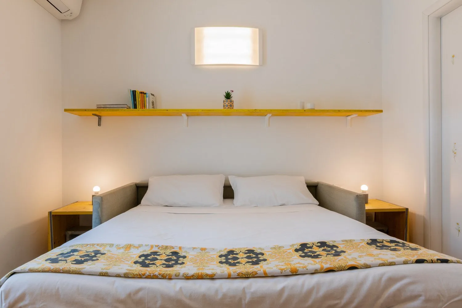 A bedroom with a double bed and a long shelf above the headboard.