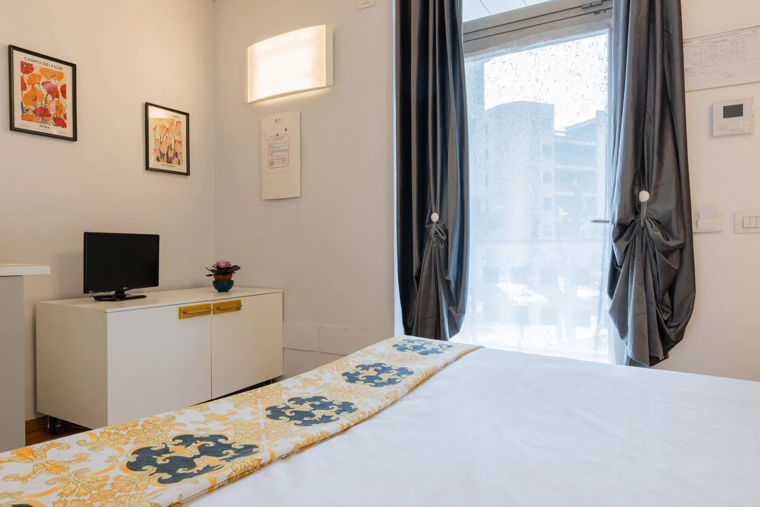 A bedroom with a bed, a television on a cabinet, and a curtained window.