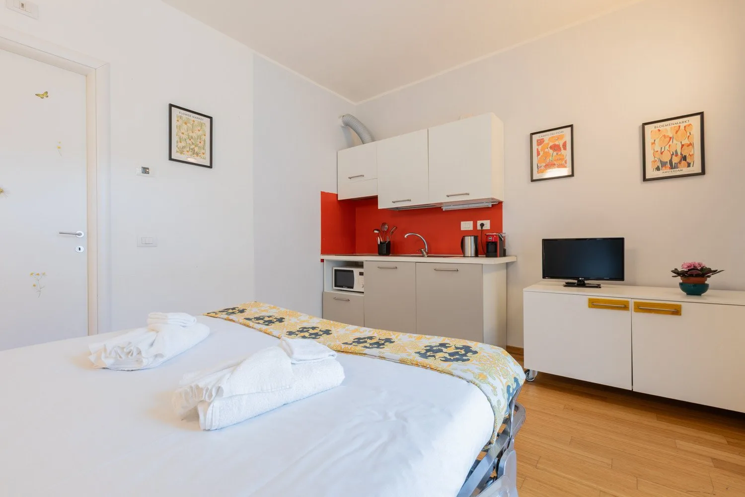 A bedroom with a kitchenette and a television on a low cabinet.