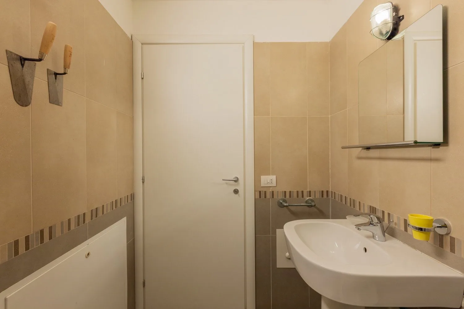 A tiled bathroom with a sink, mirror cabinet, and closed door.