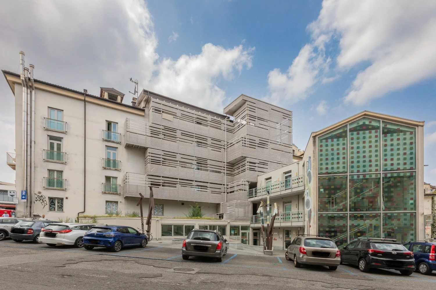 Modern multi-story building with a glass-fronted section beside a parking area.
