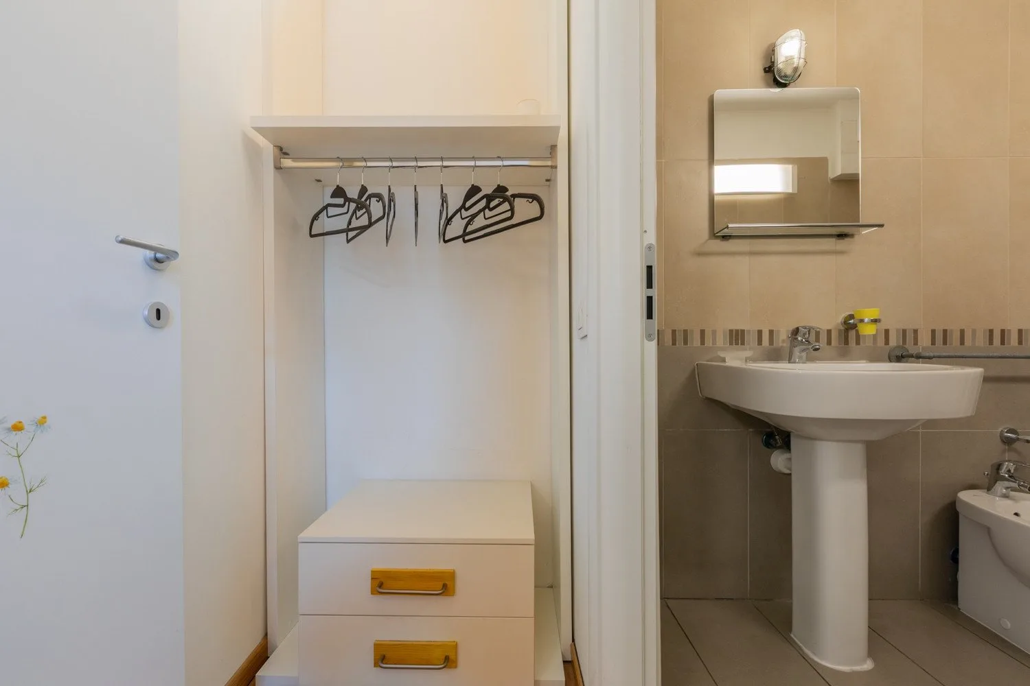 An open closet with hangers beside a bathroom sink and mirror.