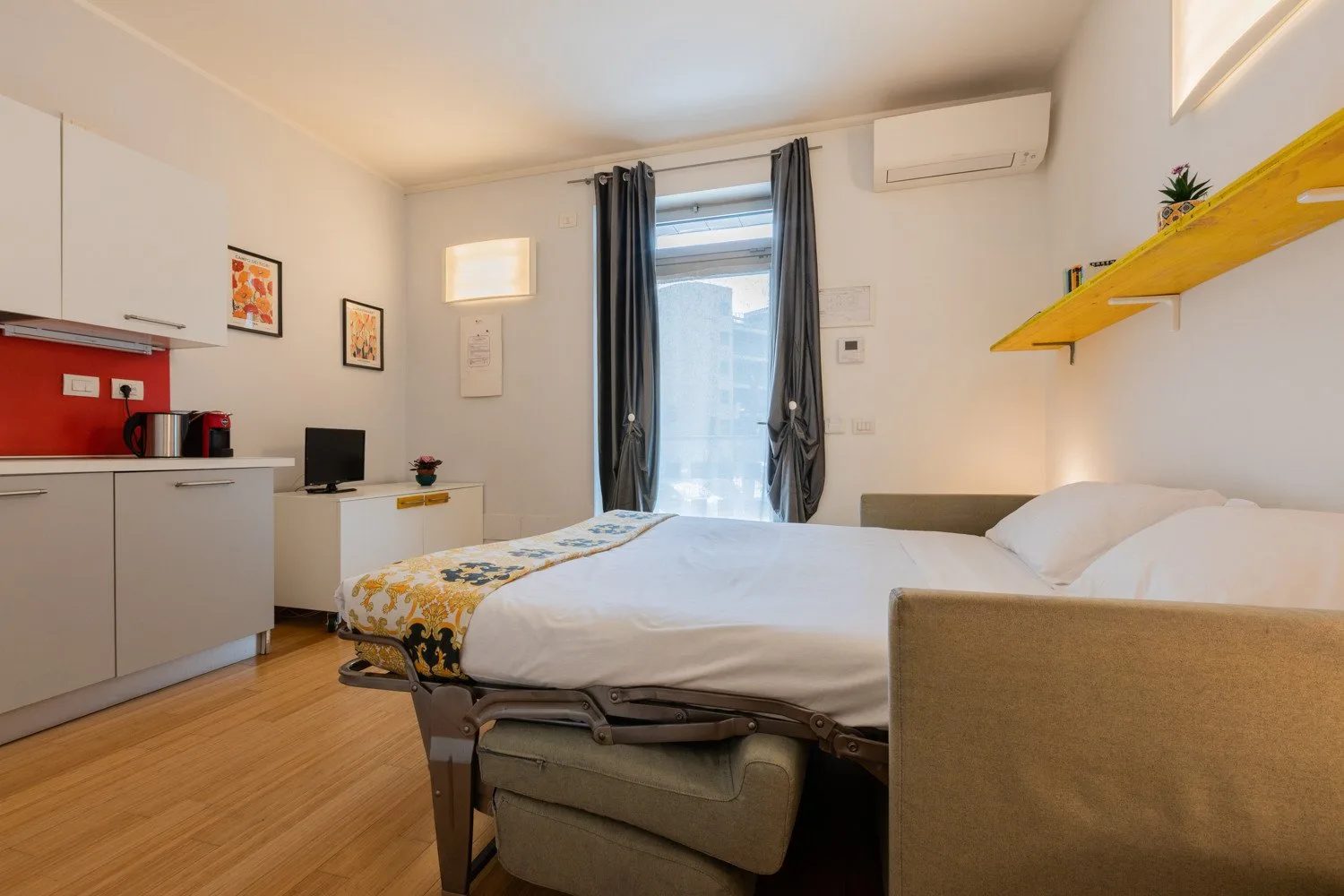 A bedroom with a bed, kitchenette, and curtained glass door.