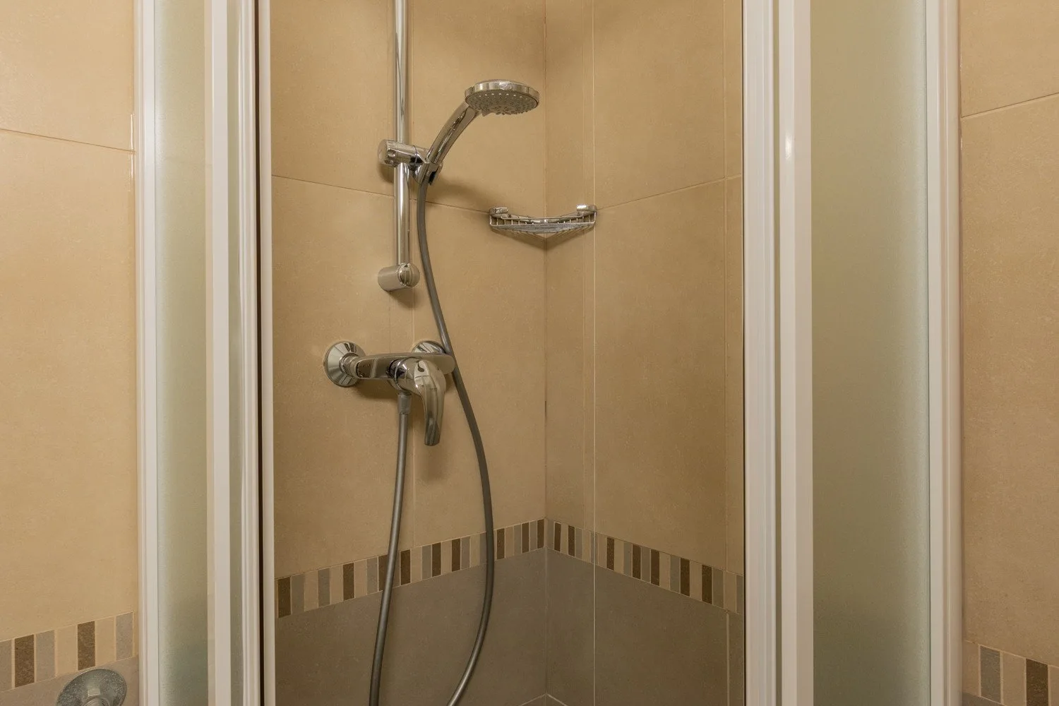 A shower with a handheld showerhead and beige tiled walls.