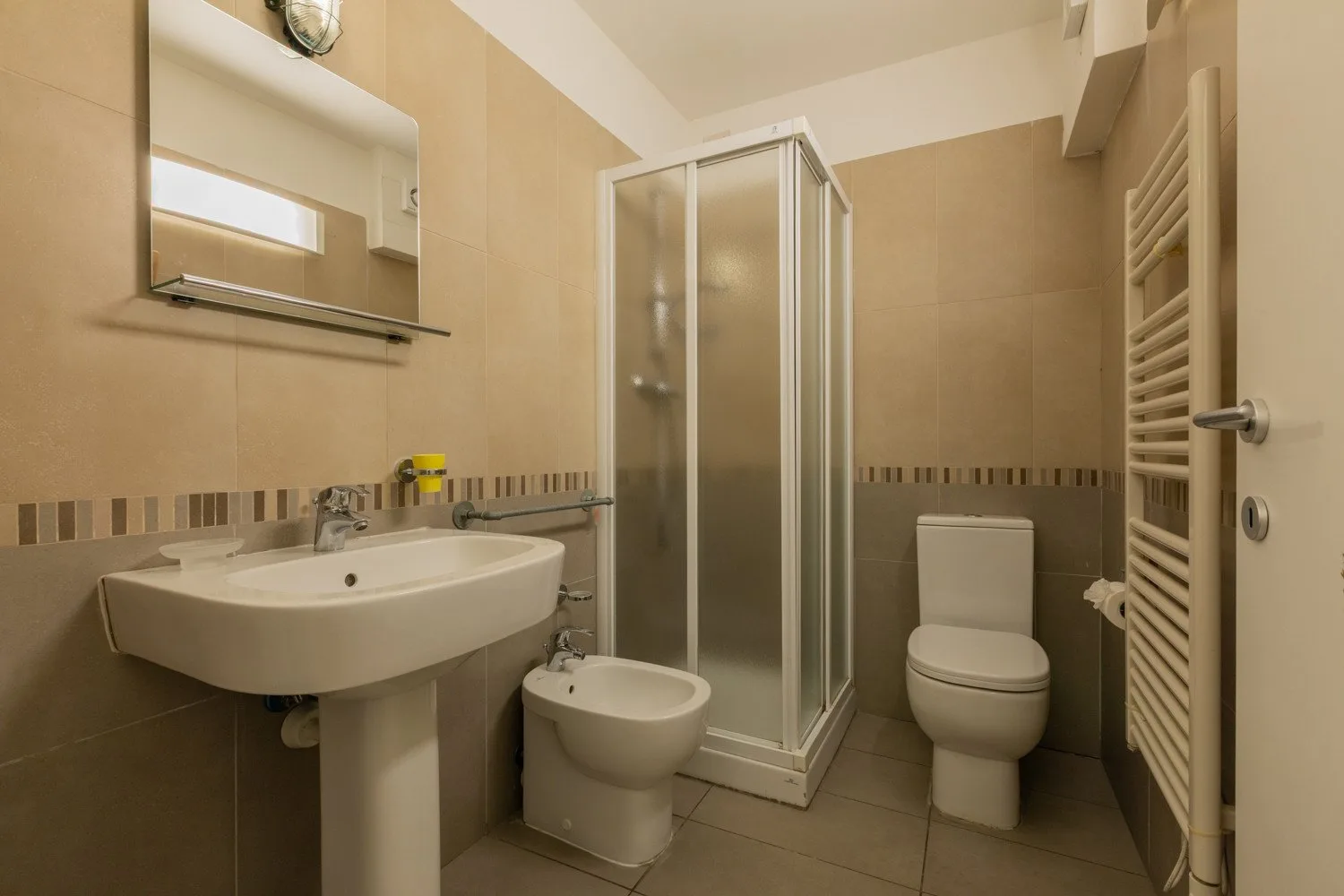A tiled bathroom with a sink, shower, toilet, and bidet.