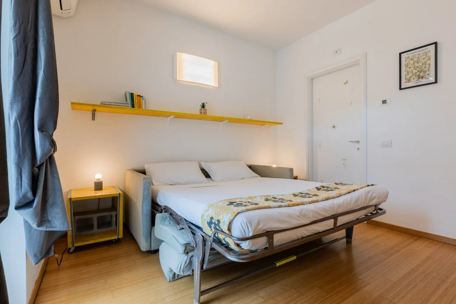 A bright bedroom with a bed beneath a long wall shelf.
