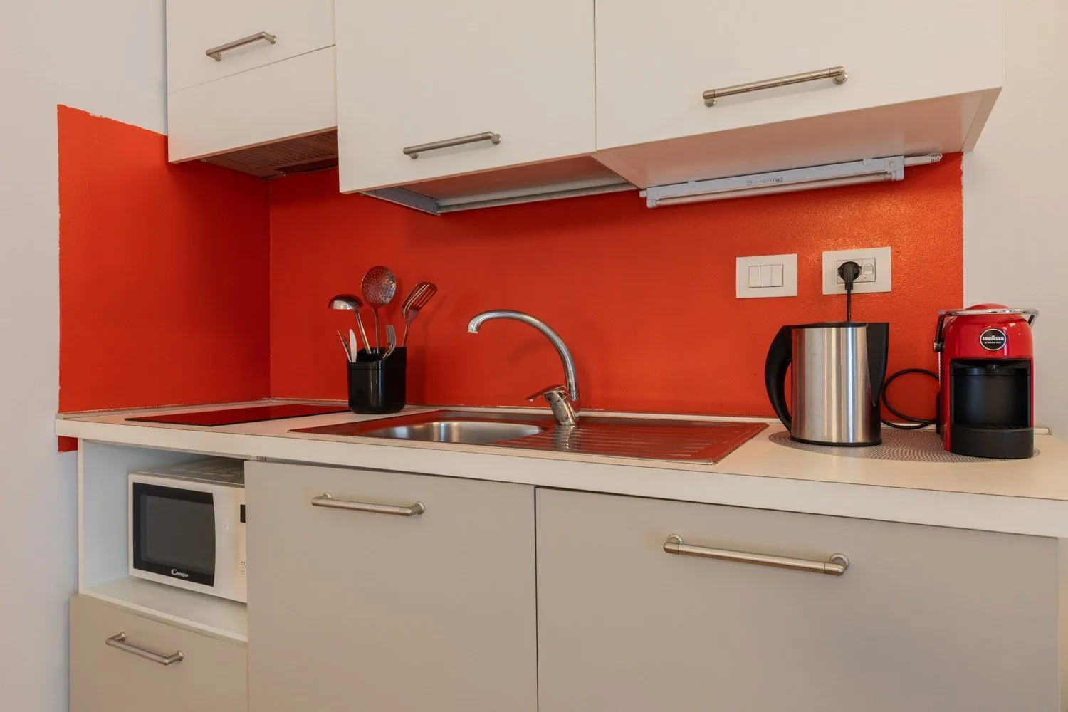 A compact kitchen with a sink, countertop appliances, and bright red walls.
