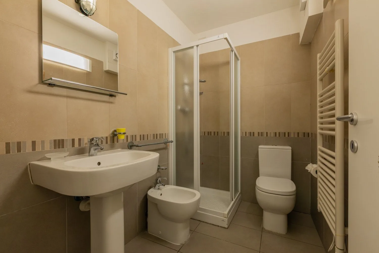 A tiled bathroom with a shower, sink, toilet, and bidet.