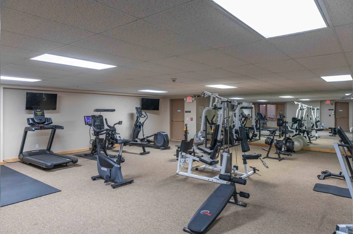 A fitness room with exercise machines and a large wall mirror.