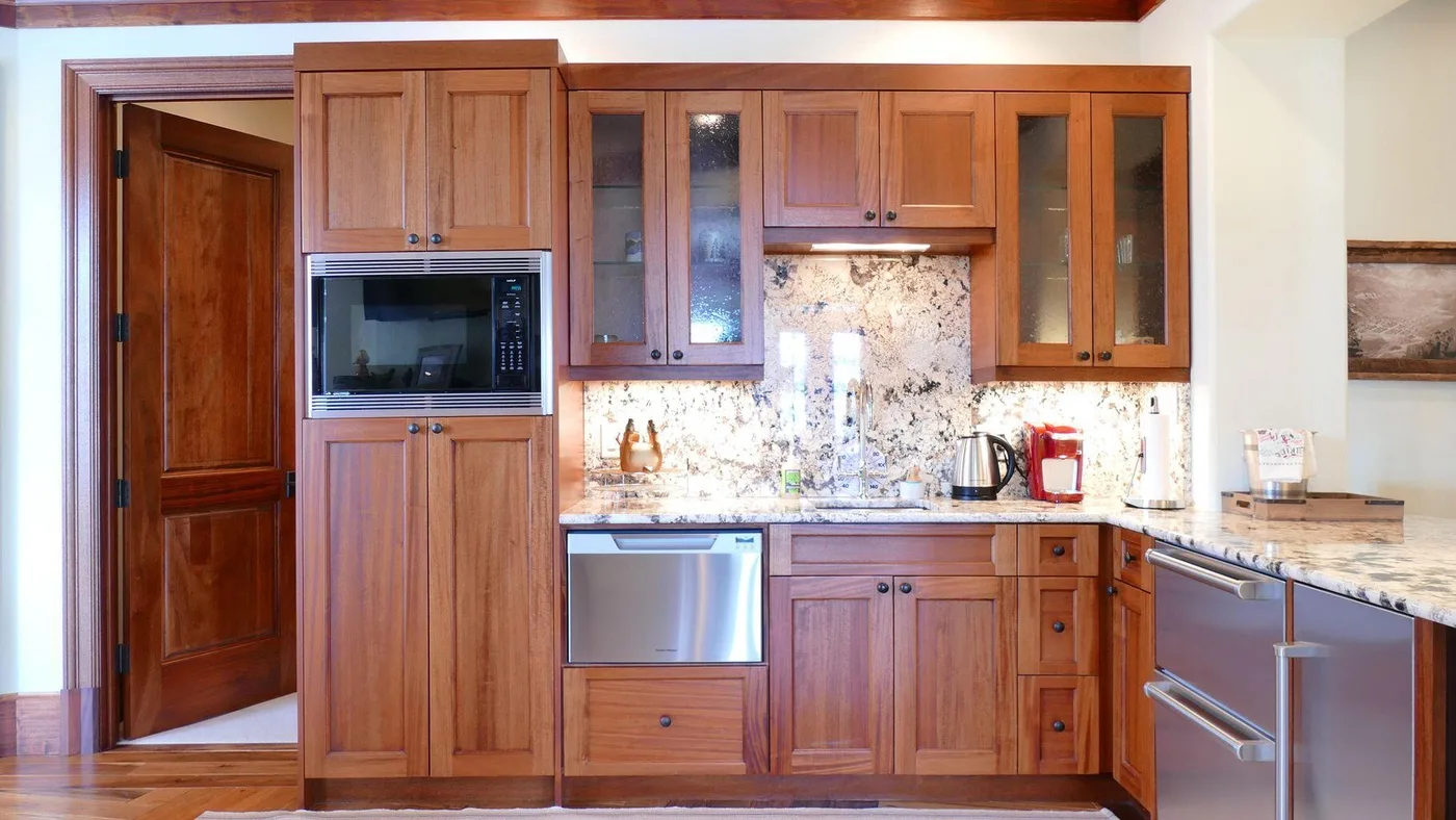 A wood-cabinet kitchen with a built-in microwave and a light stone backsplash.