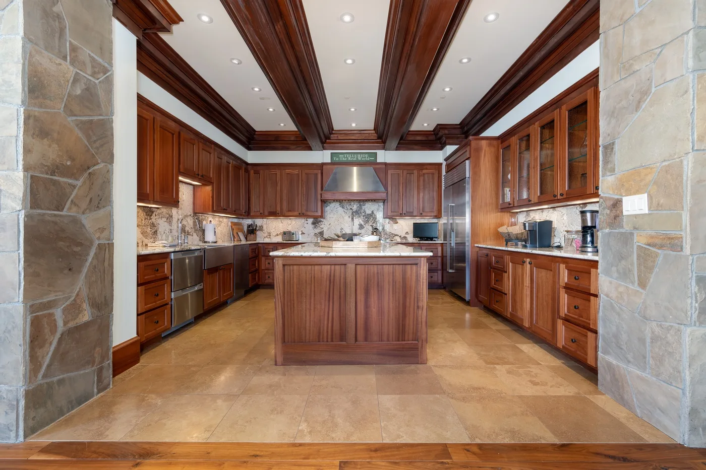 A spacious kitchen with wooden cabinets, a central island, and stone flooring.