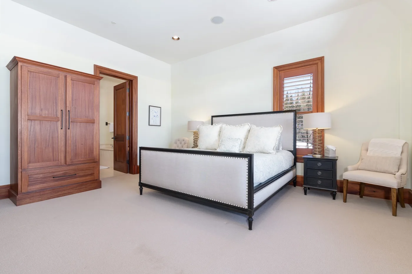 A bright bedroom with a bed, wooden wardrobe, and upholstered seating.