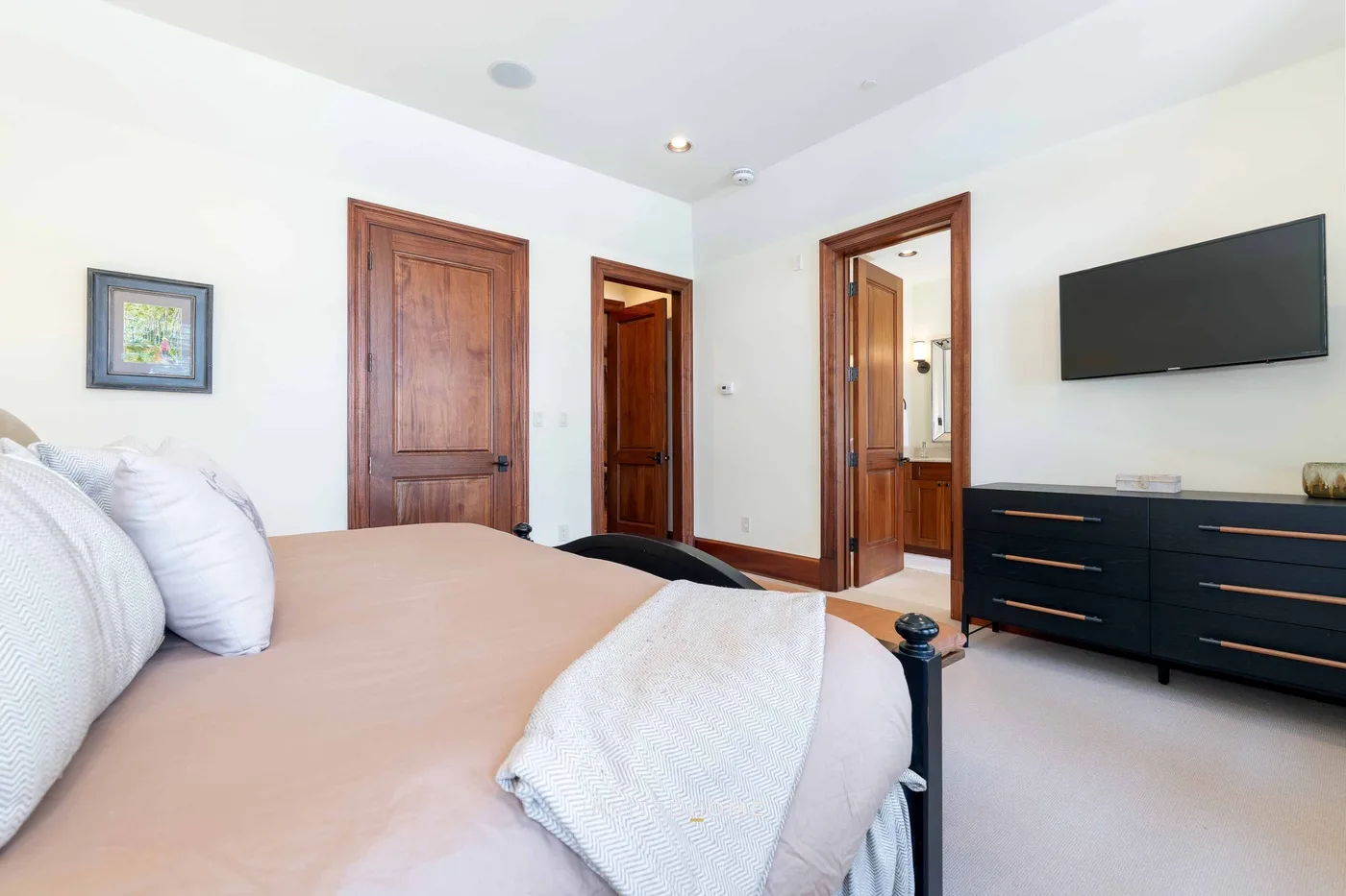 A bedroom with a bed, wall-mounted television, and dark dresser.