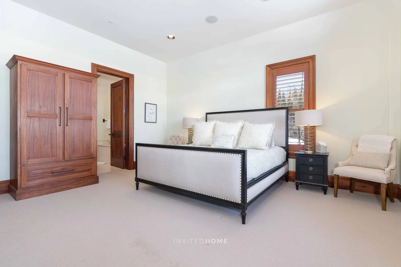 A bright bedroom with a bed, wooden wardrobe, and armchair.