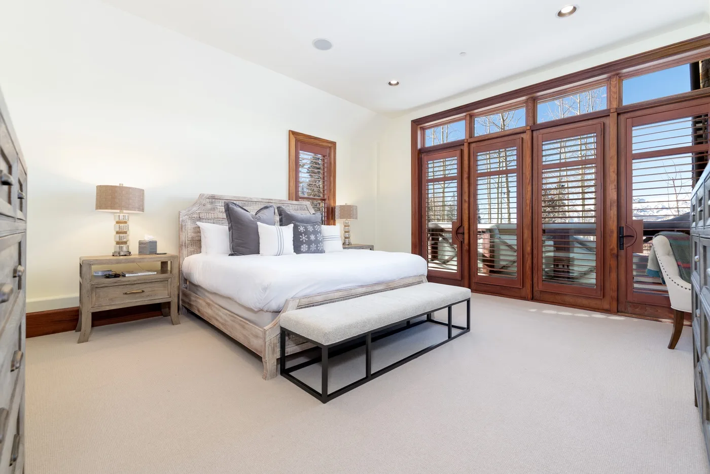 A bright bedroom with a bed, bedside table, and large wooden windows.