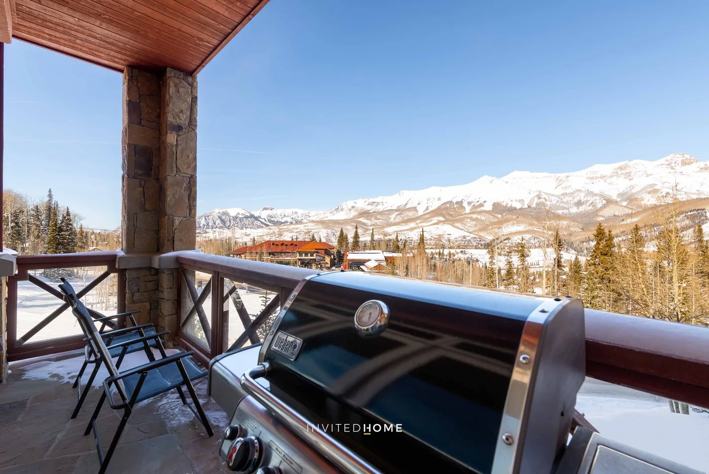 A covered outdoor terrace overlooks snow-covered mountains, with a grill and seating.