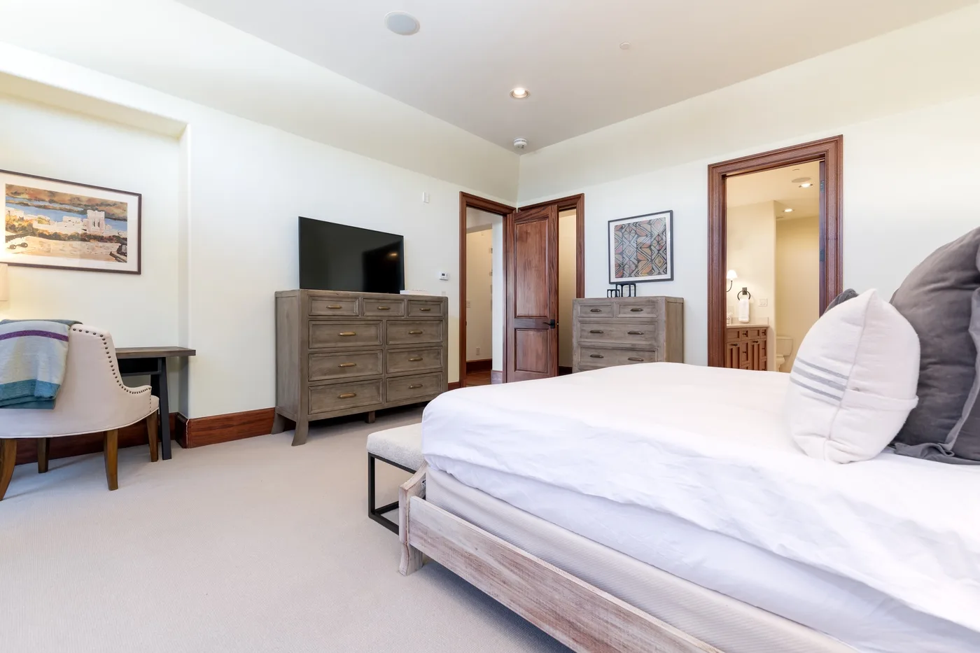 A bright bedroom with a white bed, dressers, and a television.