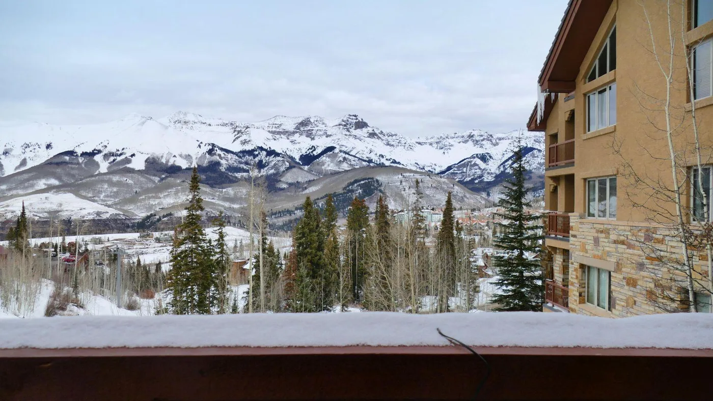 A snowy mountain landscape with evergreen trees, viewed from beside a building.