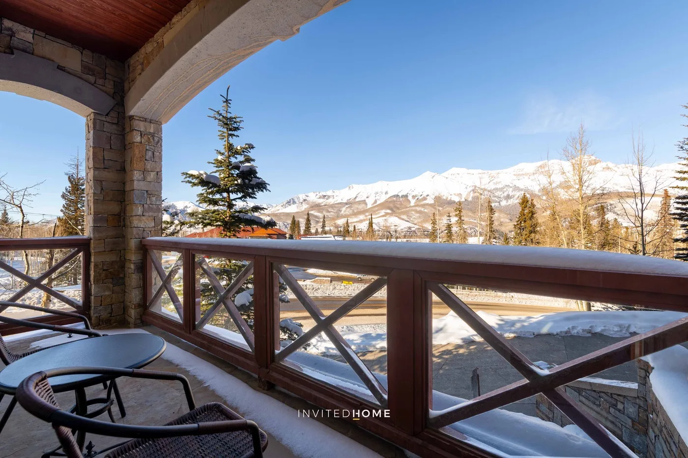 A covered balcony overlooks a snowy mountain landscape beneath a clear blue sky.