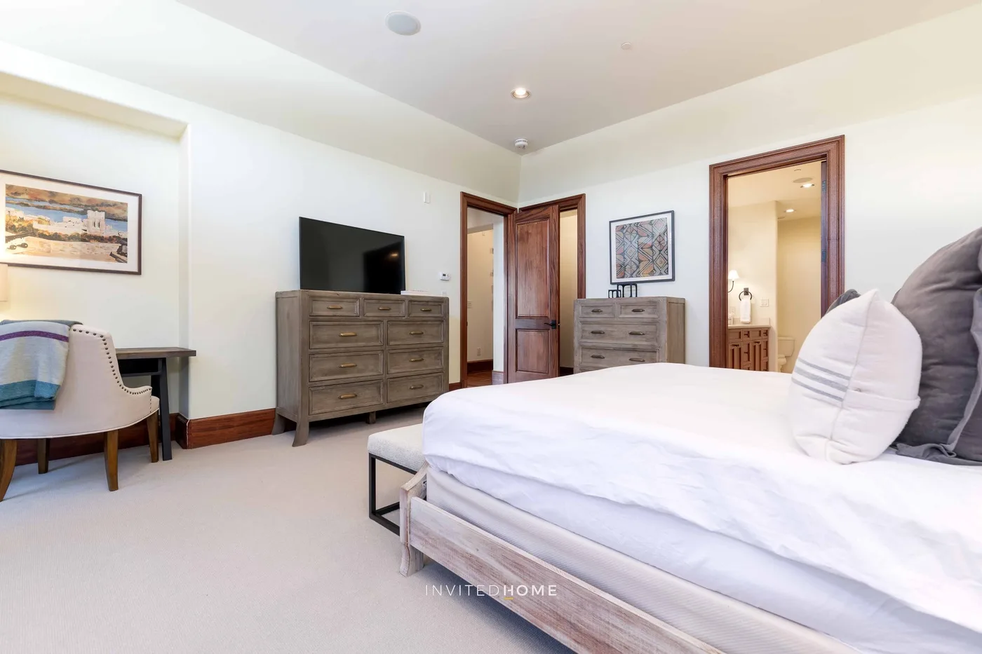 A bedroom with a large bed, wooden dressers, and a desk by the window.
