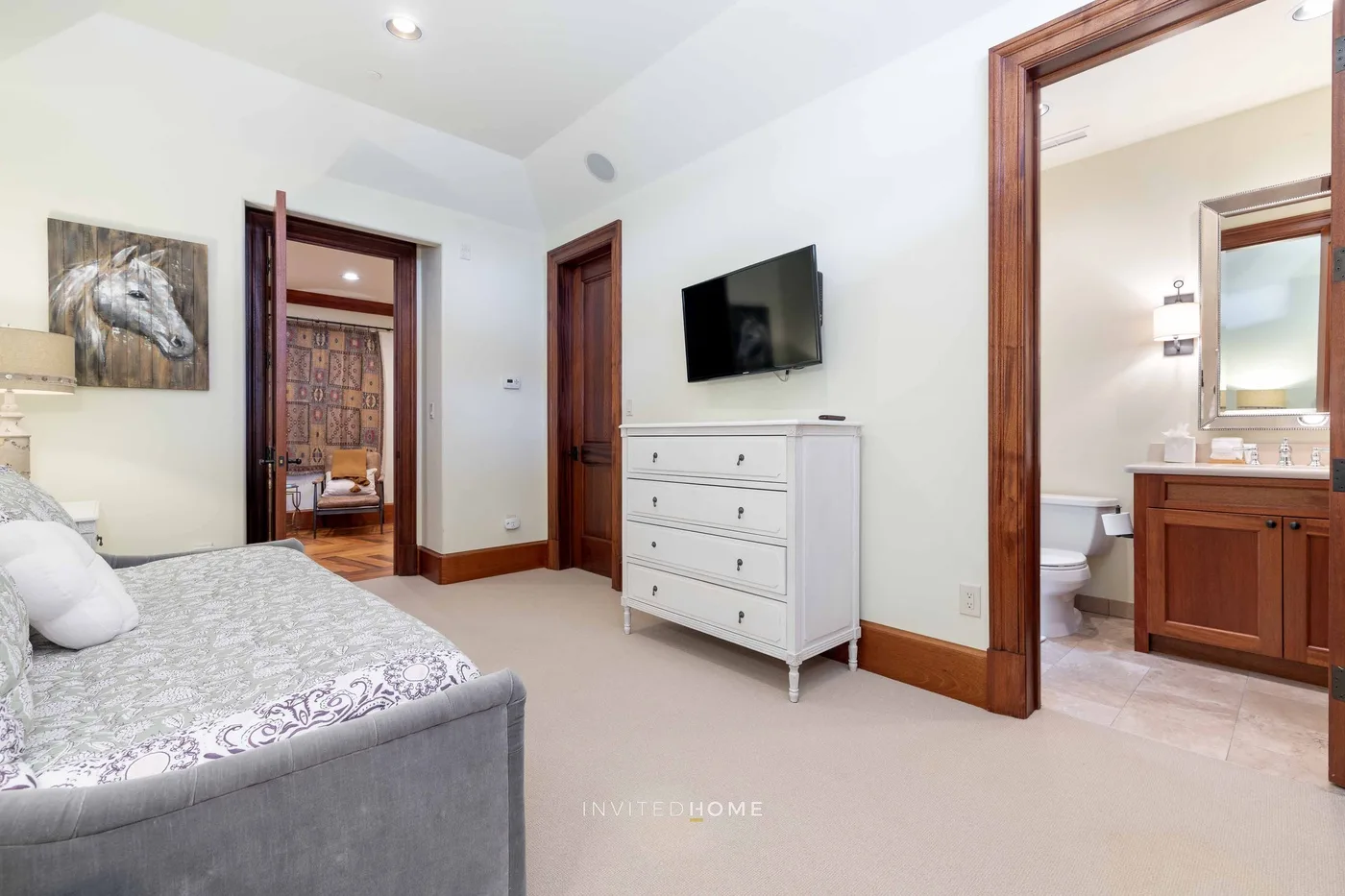 A bedroom with a bed, dresser, and television, with a bathroom visible through the doorway.