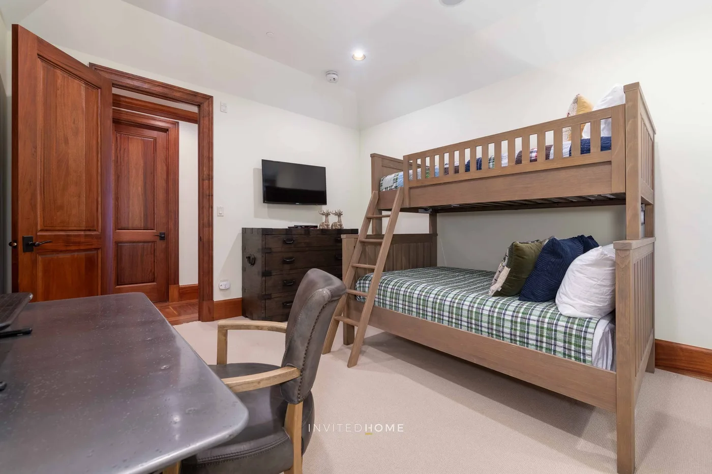 A bedroom with a wooden bunk bed, a desk, and a television.