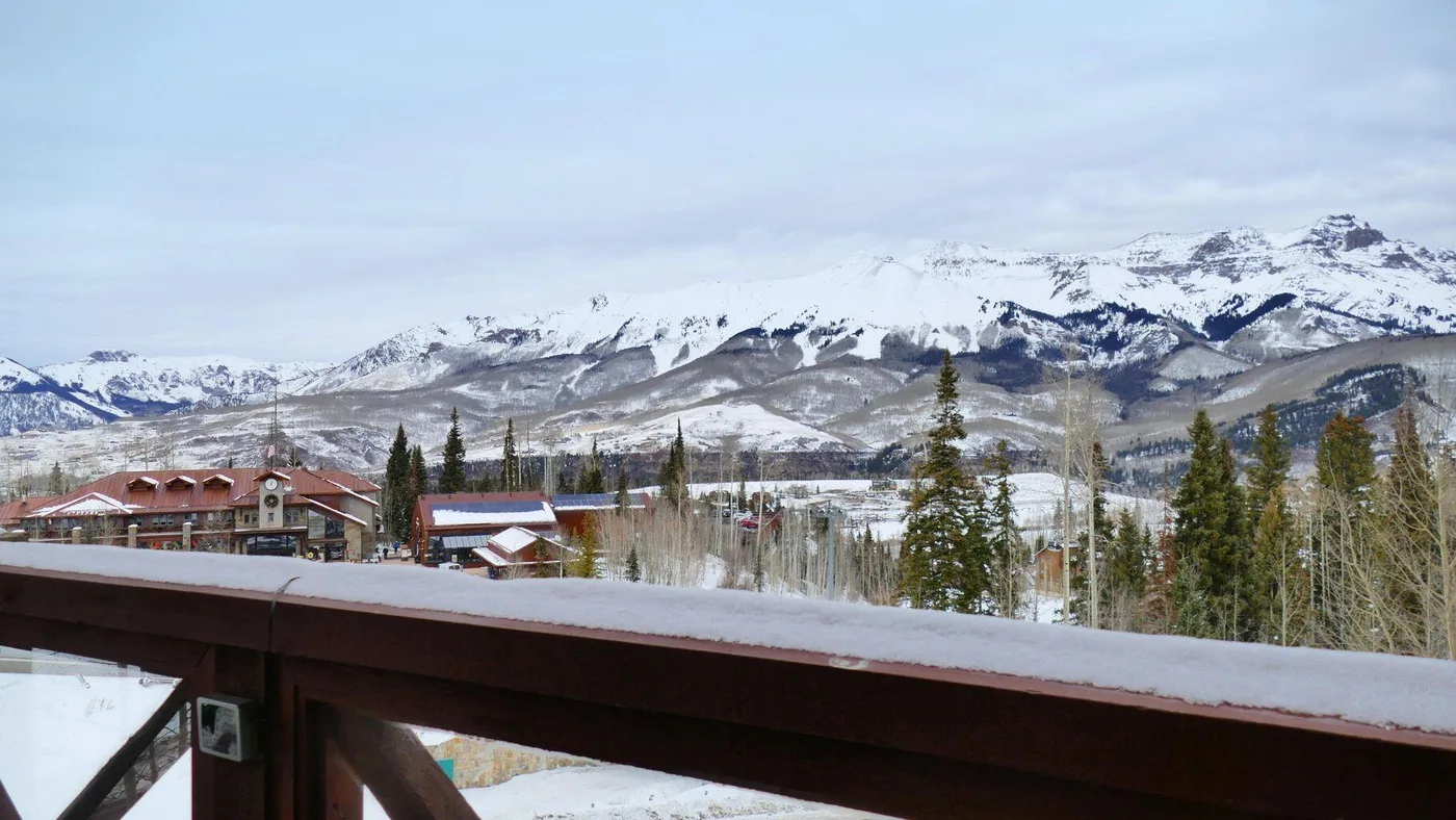A snow-covered mountain range rises behind buildings and trees.