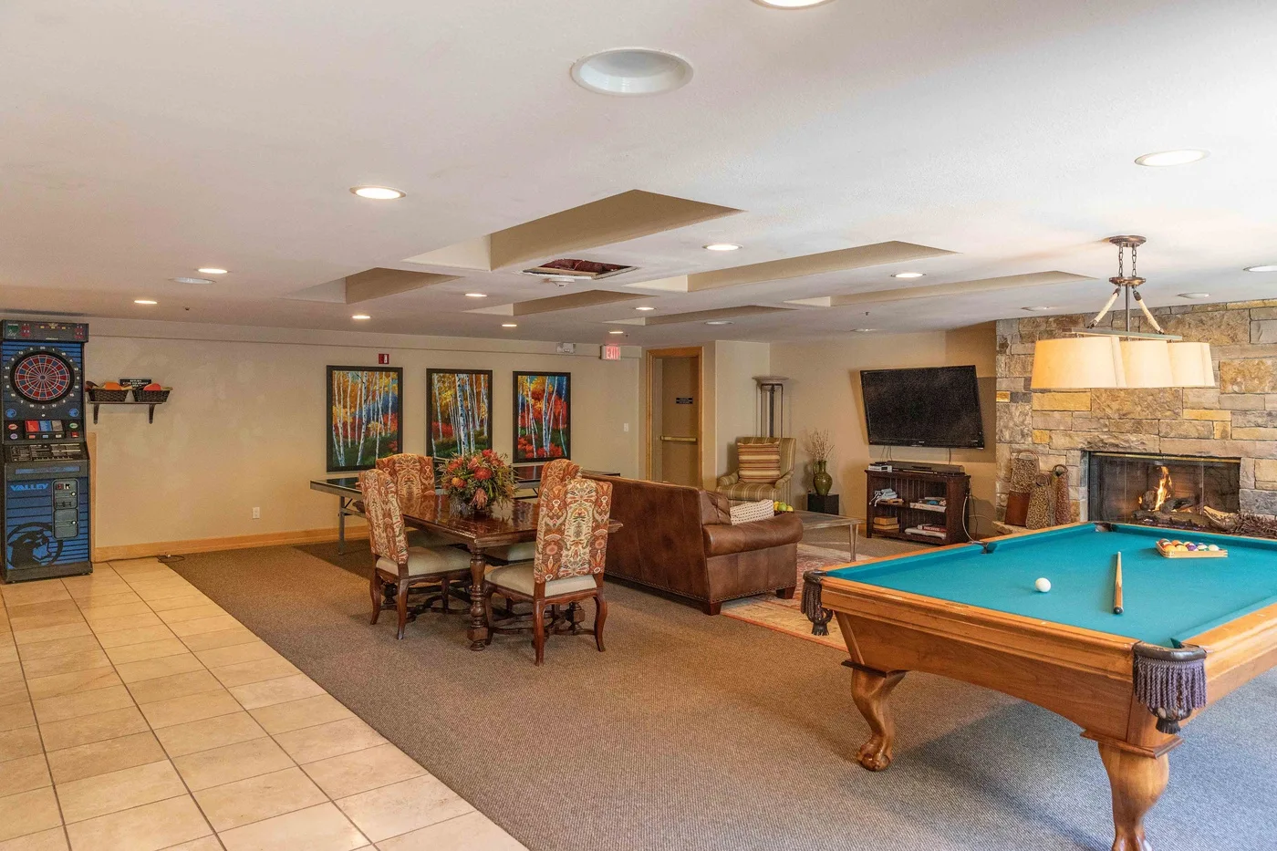 A basement recreation room with a pool table, dining area, and television.