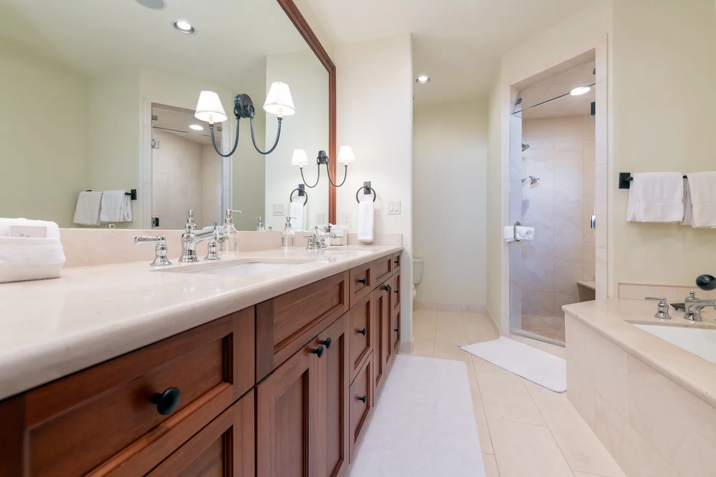 A bright bathroom with a long vanity, large mirror, and glass shower.