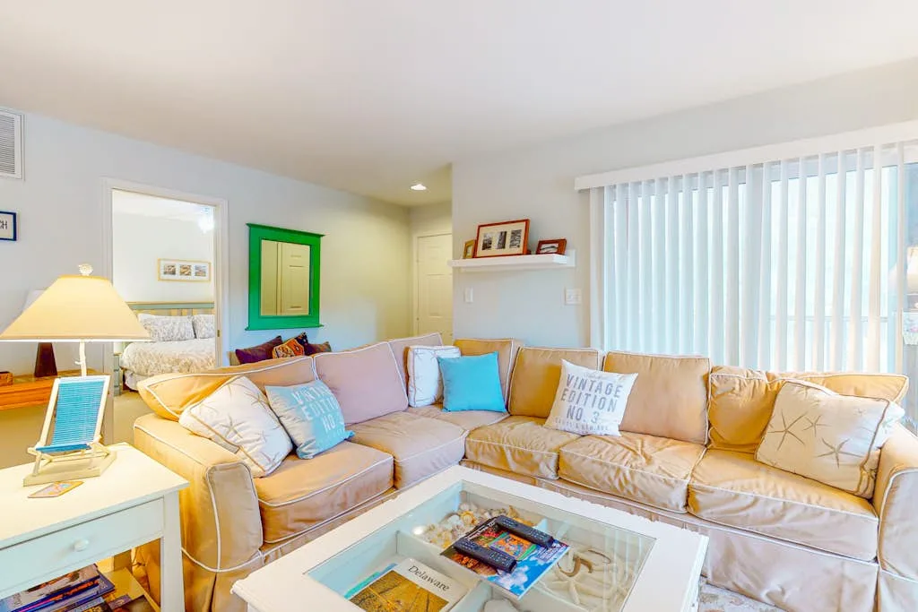 A bright living room with sectional seating, colorful cushions, and a glass coffee table.