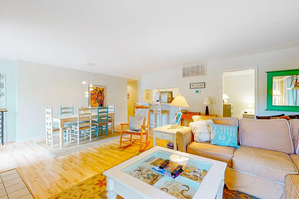 A bright living room with seating around a coffee table and dining area beyond.