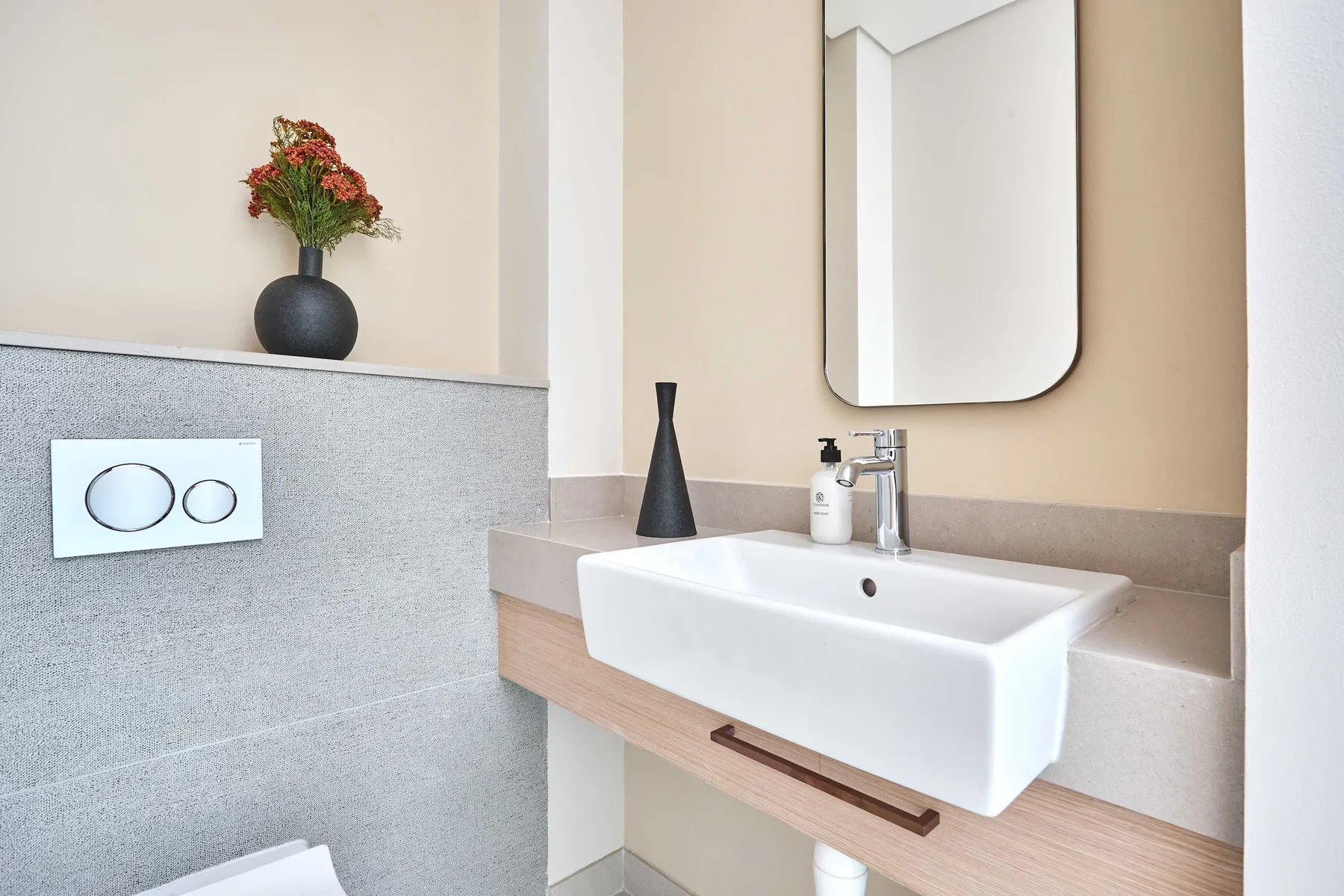 A bathroom vanity with a white sink, wall mirror, and flowers in a vase.