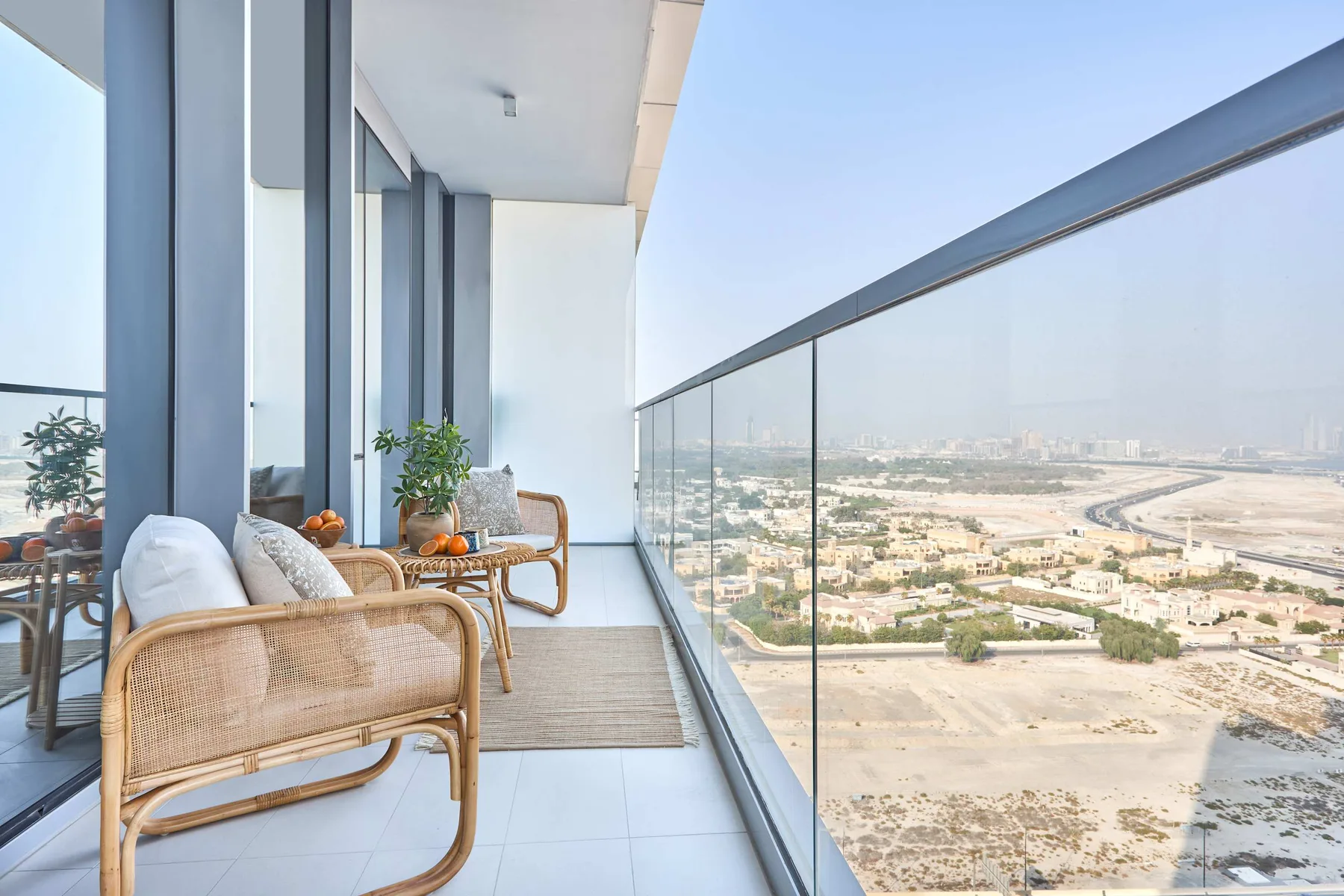 A balcony with seating and a glass railing overlooks a broad cityscape.