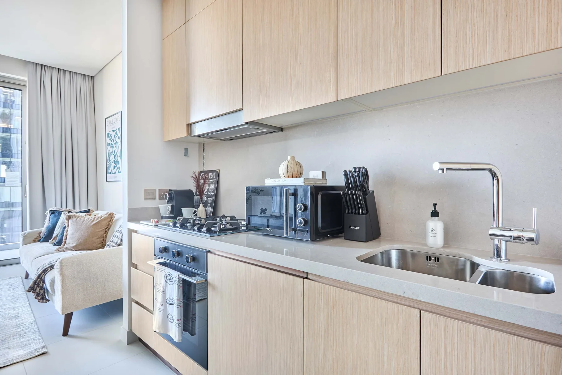 A bright kitchen with a long counter, sink, and cooking area beside a seating space.