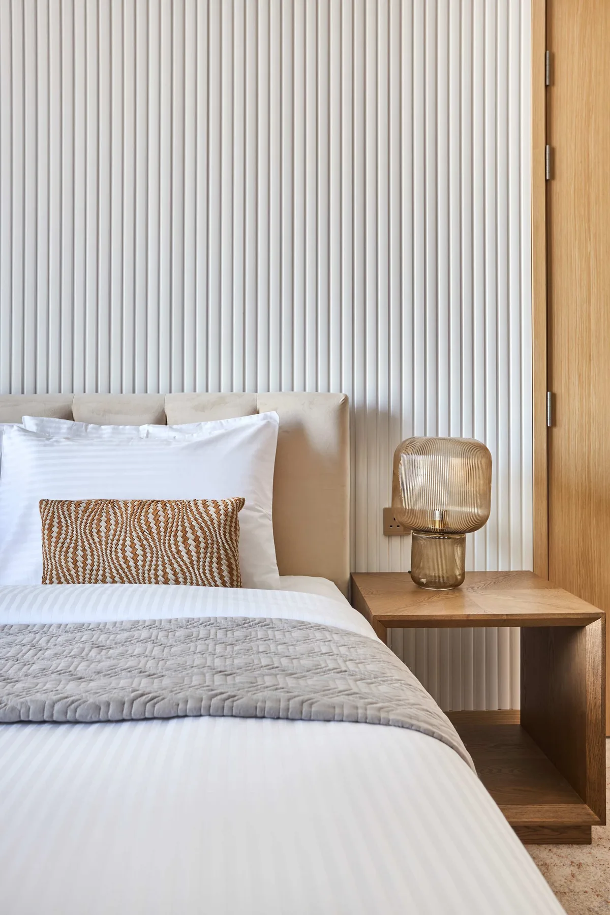 A bedroom with a neatly made bed and a wooden bedside table.