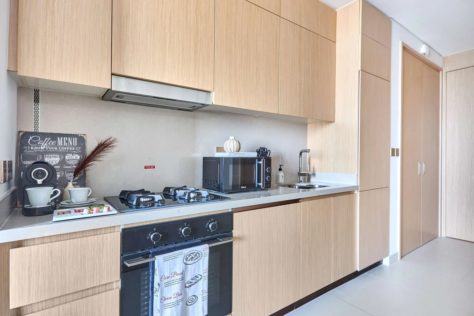 A modern kitchen with light wood cabinets, a cooktop, and an oven.