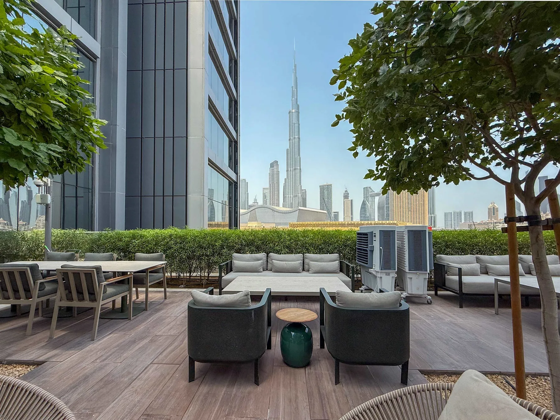An outdoor terrace with seating and a city skyline beyond the trees.