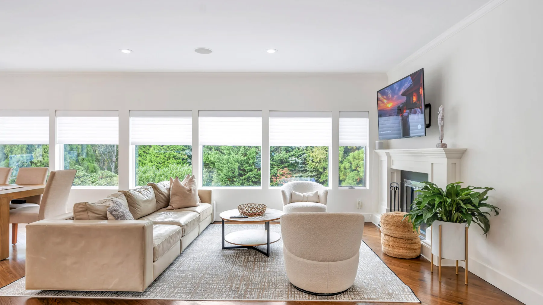 Una sala luminosa tiene un sofá, sillones y un televisor junto a amplias ventanas.