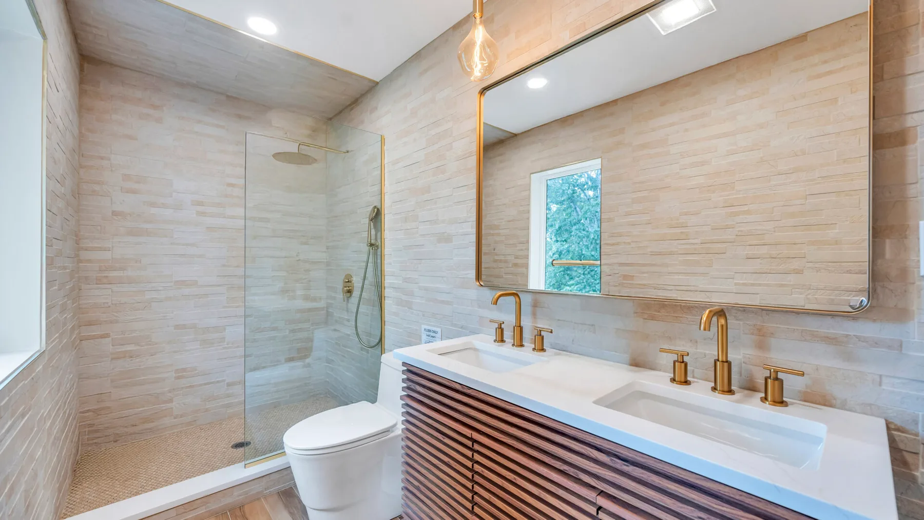 Baño revestido de azulejos con ducha de vidrio, inodoro y lavabo doble.