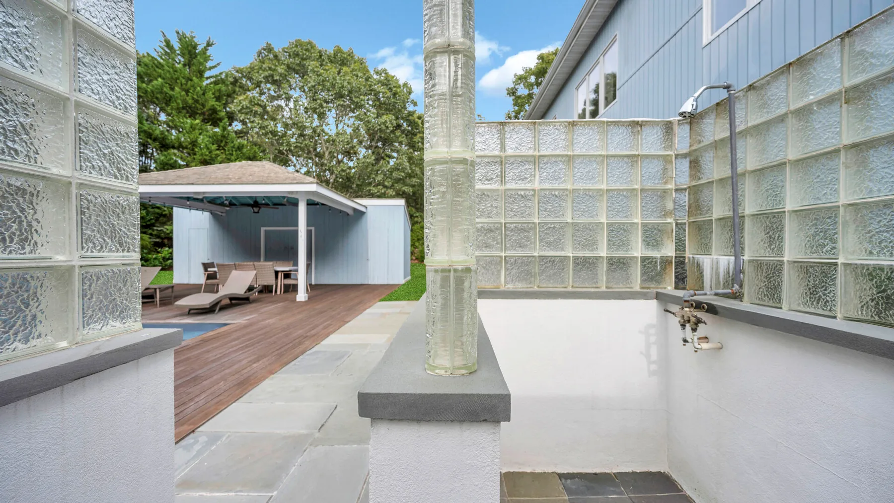 Un patio moderno con una tarima de madera, paredes de bloques de vidrio y asientos al aire libre.