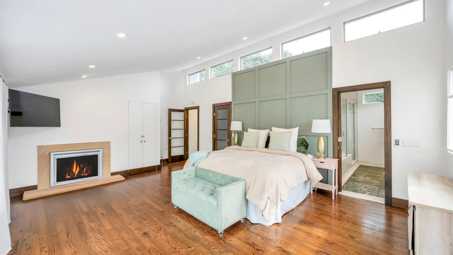 Un dormitorio luminoso con una cama, asientos verde claro y suelo de madera.