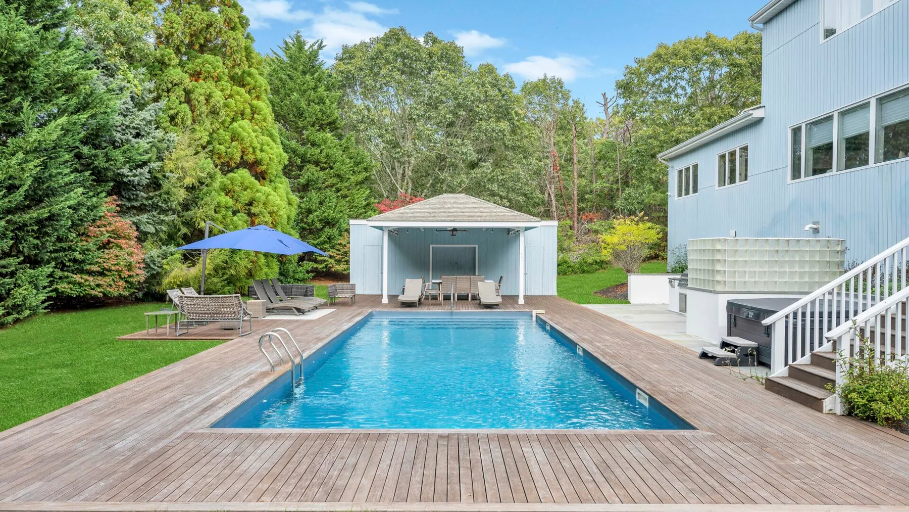 Una piscina al aire libre está junto a una terraza, con una zona de estar cubierta al fondo.
