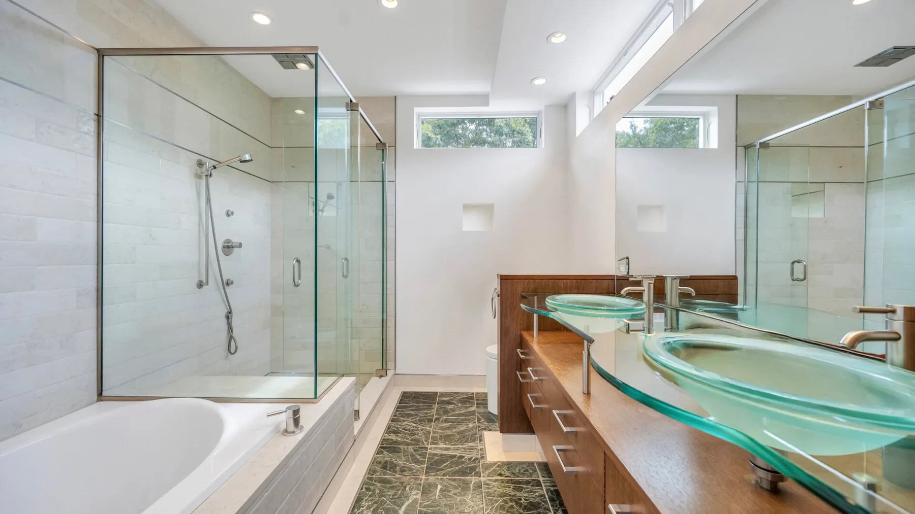 Un baño luminoso con bañera, ducha de vidrio y un largo tocador.