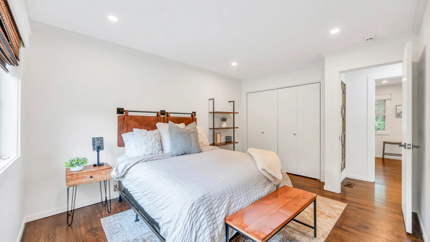 Un dormitorio luminoso con una cama, una mesa auxiliar y suelo de madera.