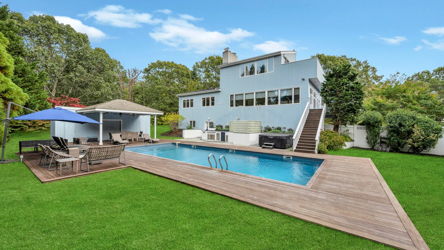 Una piscina y una terraza de madera están junto a una casa moderna y un césped verde.
