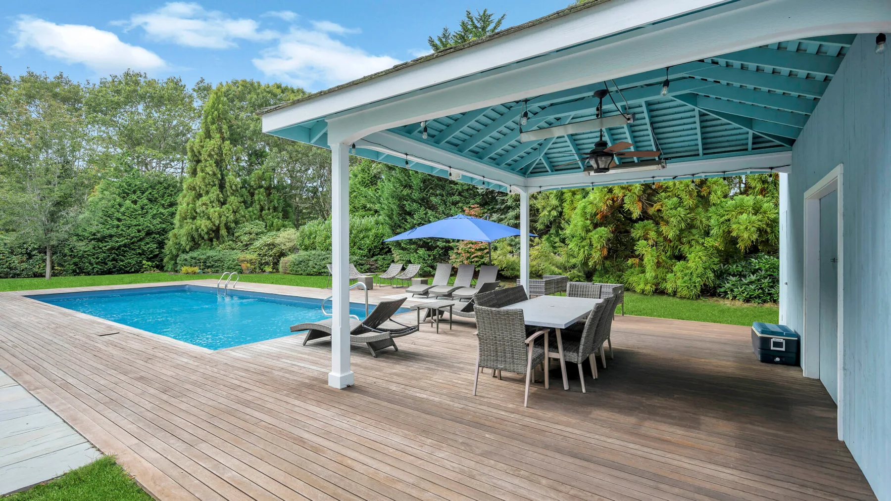 Un patio cubierto con asientos al aire libre da a una piscina y un paisaje verde.