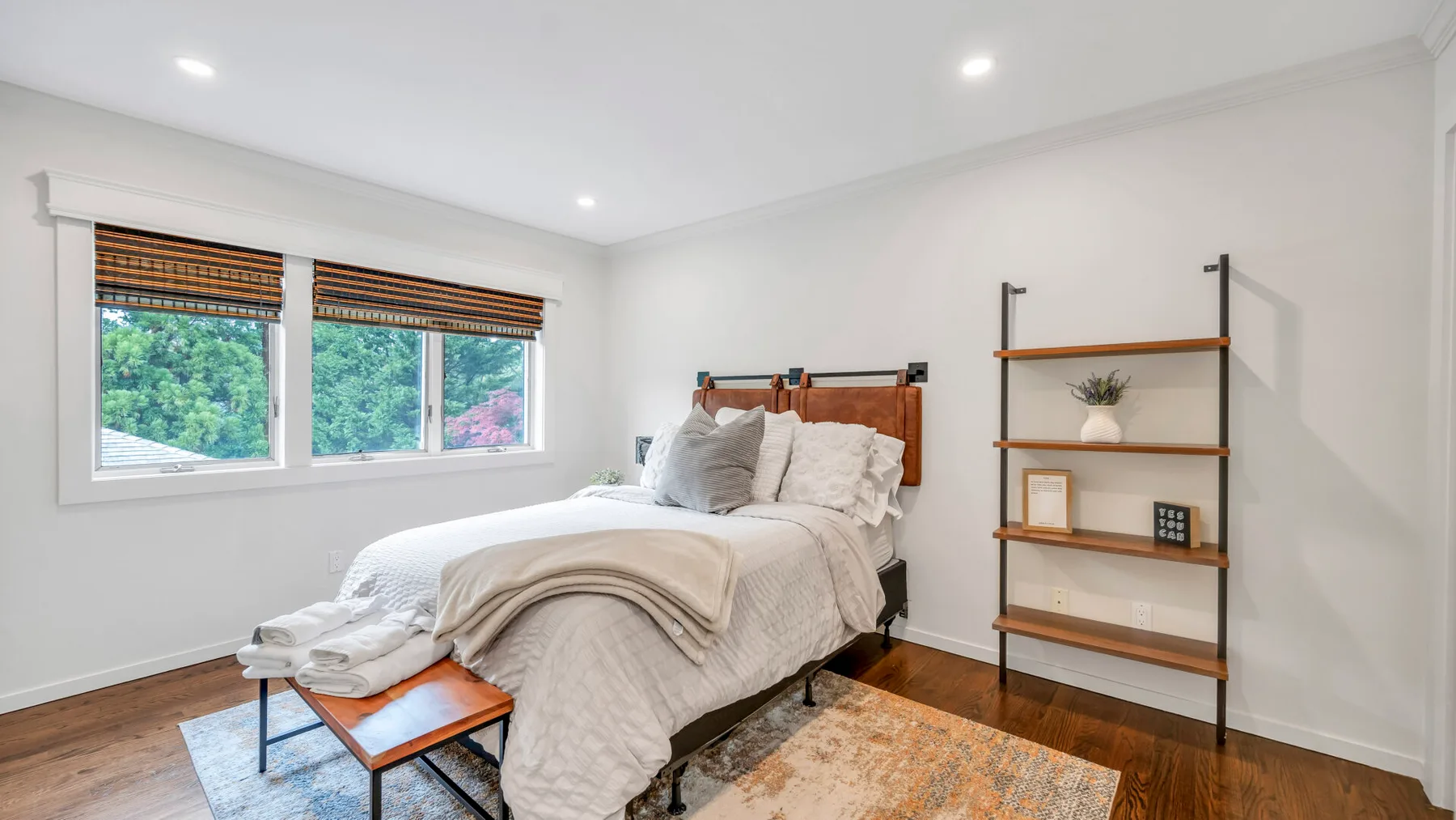 Un dormitorio luminoso con una cama tendida y ventanas con vistas a la vegetación.