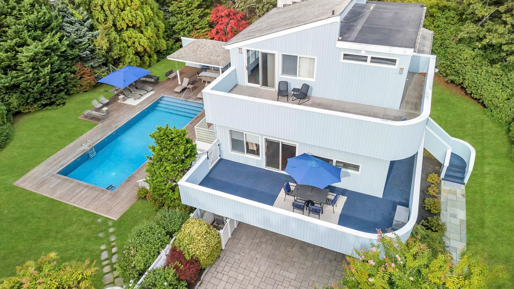 Una casa moderna con dos terrazas al aire libre junto a una piscina y un jardín verde.